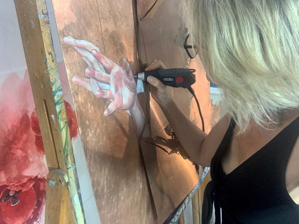 Liz Gray working in her studio on a copper art painting